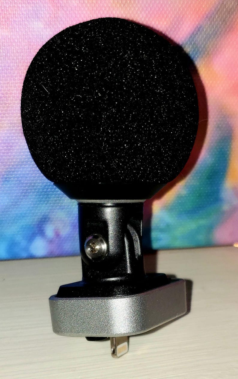 May include: A black microphone with a rounded, foam head. The microphone has a silver base and a black stem. The base has a lightning connector. The background is a colorful tie-dye pattern.