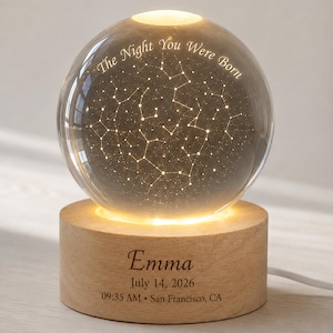 May include: A clear glass sphere lamp featuring an engraved star constellation map and the text The Night You Were Born. The sphere rests on a cylindrical light-up wooden base engraved with the name Emma, July 14, 2026, 09:35 AM, and San Francisco, CA.