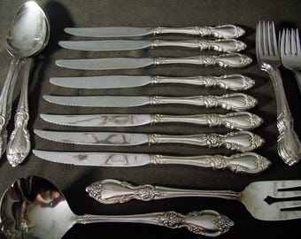 May include: A set of silverware with ornate handles. The set includes a soup spoon, a butter knife, and several dinner forks and knives.