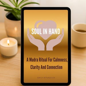 May include: A tablet displays the text "SOUL IN HAND" above a heart and hands graphic. Below, it reads "A Mudra Ritual For Calmness, Clarity And Connection" and "DAILY RITUALS CO". A lit candle, a plant, and a mug are in the background.