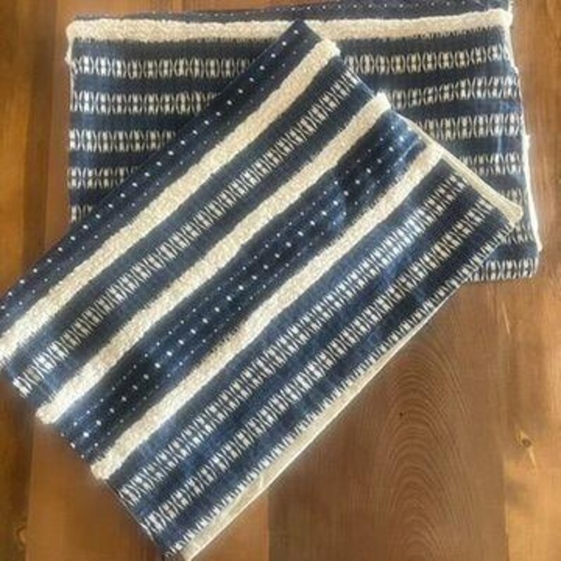 May include: Two blue and white patterned throw pillows. The pillows have a striped design with white and blue vertical stripes. The top pillow is folded in half. The pillows are on a wooden surface.