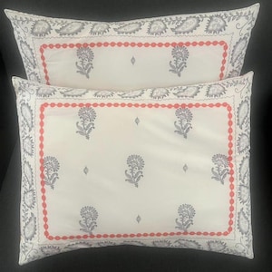 May include: Two rectangular decorative pillows. The pillows have a white background with a floral pattern in gray and a red beaded border. The edges of the pillows have a gray paisley design.