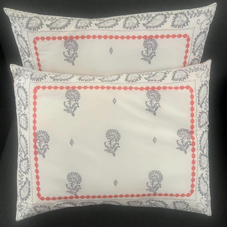 May include: Two rectangular decorative pillows. The pillows have a white background with a floral pattern in gray and a red beaded border. The edges of the pillows have a gray paisley design.