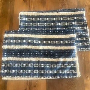 May include: Two rectangular throw pillows with a blue and white striped pattern. The pillows have a textured appearance with a combination of horizontal stripes and dotted designs. The pillows are placed on a wooden surface.