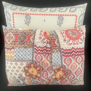 May include: Two decorative throw pillows with intricate patterns. The top pillow has a cream background with a red border and floral designs. The bottom pillow features a mix of floral and geometric patterns in red, orange, blue, and yellow.