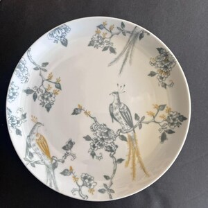 May include: White ceramic plate with a bird and floral design. The plate features two birds perched on branches with gray and gold accents. The floral pattern includes gray and gold flowers and leaves, creating an elegant aesthetic.