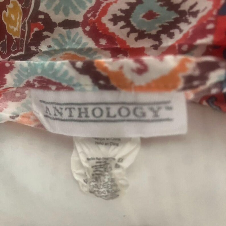 May include: Close-up of a fabric with a colorful, intricate pattern in shades of red, blue, orange, and white. The fabric has a tag that reads "ANTHOLOGY".