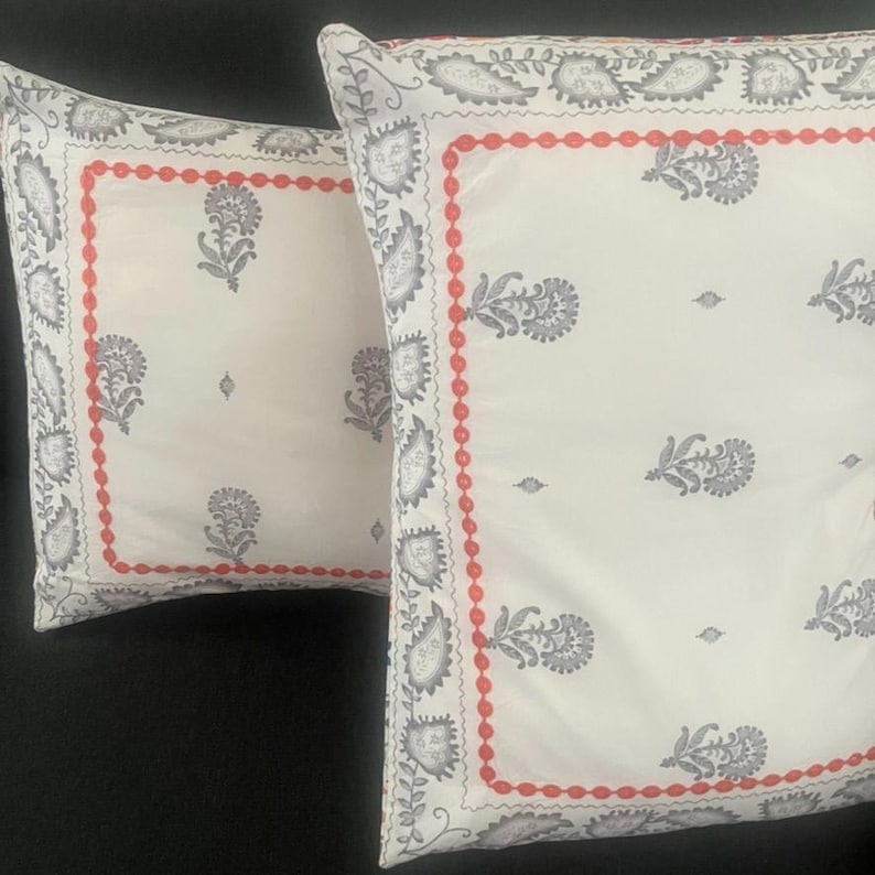 May include: Two square throw pillows with a white background. Each pillow features a gray floral pattern and a red border. The pillows are made of a soft fabric and are suitable for a bed or sofa.