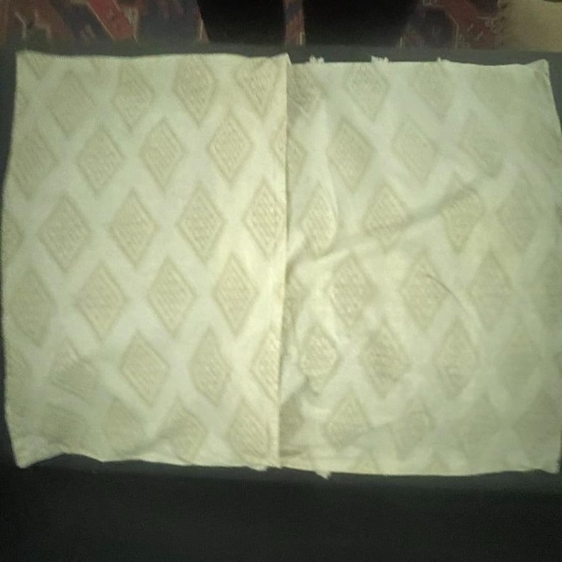 May include: Two off-white pillow covers with a repeating diamond pattern. The diamonds are outlined in a slightly darker shade, creating a subtle contrast. The fabric appears to have a textured weave, adding visual interest to the design.