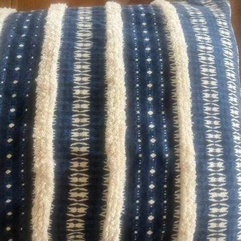 May include: A decorative pillow with a textured design. The pillow features vertical stripes of cream-colored, raised fabric alternating with navy blue stripes. The navy stripes have a dotted and patterned design.