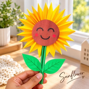 May include: A paper craft sunflower featuring bright yellow pointed petals, a brown circular center with a black smiling face and pink cheeks, and two green paper leaves attached to a green stem. The word Sunflower is written in cursive.