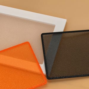 May include: Three rectangular mesh sheets with rounded corners. One sheet is white with a fine beige grid, one is bright orange with a fine grid, and one is black with a fine grid. The sheets are layered partially over one another.