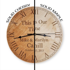 May include: A wooden clock with Roman numeral markings and the text "This Is Our Time" engraved on the face. The clock is personalized with the names "Mike & Marilyn Cahill" and the date "October 03, 2015". The clock is shown in two wood finishes: solid cherry and solid maple.