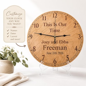 May include: A personalized wooden clock with black hands and a light wood grain finish. The clock face reads "This Is Our Time," with the names "Joey and Ebba Freeman" and the date "June 26th 2026." A sign on the left says "Customize your clock any way you want!"