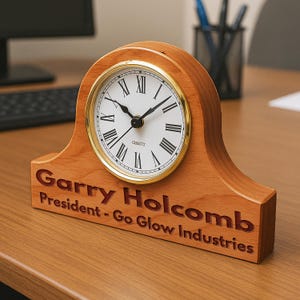 May include: A wooden desk clock with a gold-rimmed face and Roman numeral markings. The clock is engraved with the name "Garry Holcomb" and the title "President - Go Glow Industries".