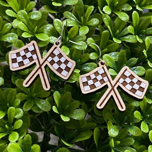 May include: A pair of wooden earrings featuring a checkered flag design. The flags are crossed and the earrings are silver.