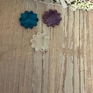 May include: Three decorative flower-shaped resin embellishments in teal, purple, and white.