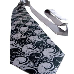 Puede incluir: Una corbata plateada con un patrón repetido de ilustraciones de pulpos en blanco y negro. La corbata está hecha de una tela suave y se muestra sobre un fondo blanco. El diseño de pulpo añade un toque único y elegante.