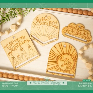 May include: Four wooden phone stand designs with laser cut designs and text. The designs include a sun with the text "hello sunshine", a cloud with the text "good vibes only", a sun with the text "let's just go", and mountains with the text "take me to the mountains".