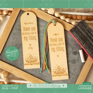Può includere: Due segnalibri in legno con un design a libro aperto con fiori tagliato al laser e il testo "Grazie per essere parte della mia storia". Un segnalibro ha il testo "Miss Thoms" e "Lily".