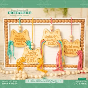 May include: Four wooden cat-shaped ornaments with different sayings: "Sorry I'm late, I saw a cat", "Hold on, I see a cat", "Hold on, I see a cat", and "Sorry I'm late, I saw a cat". Each ornament has colorful yarn tassels.