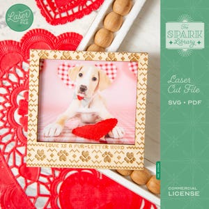 May include: A wooden picture frame with a photo of a puppy wearing a bow tie and holding a red heart. The frame has paw prints and the text "LOVE IS A FUR-LETTER WORD". The image also includes red heart-shaped decorations.