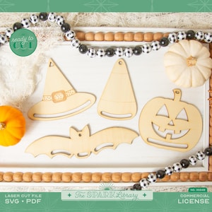 May include: Wooden Halloween-themed cutouts, including a witch hat, candy corn, jack-o'-lantern, and bat, arranged on a white tray with decorative beads and pumpkins. The text "ready to cut" and "The Spark Library" are visible.