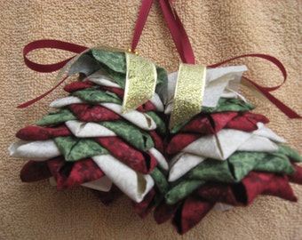 May include: Two handmade fabric Christmas tree ornaments with red, white, and green fabric. The ornaments are tied with red ribbon and gold ribbon.