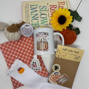 Könnte beinhalten: Eine Sammlung von Gegenständen, darunter ein Buch mit dem Titel Slow Dance, eine weiße Tasse mit einem Autumn Reading Kürbis-Motiv, weiße Socken mit Kürbisstickerei, ein gehäkelter Kürbis, eine Sonnenblume und ein Fall Feels Aufkleber-Set.