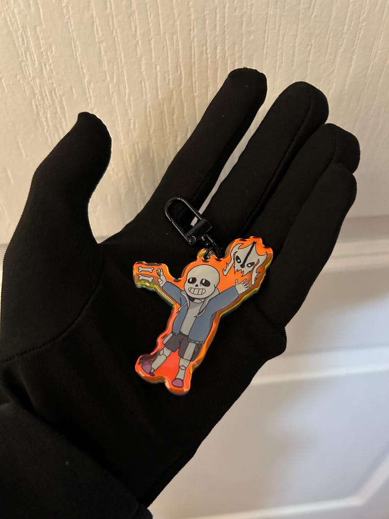 K&ouml;nnte beinhalten: Ein farbenfroher Acryl-Schl&uuml;sselanh&auml;nger mit einer Cartoonfigur in einer blauen Jacke, grauen Shorts und orangefarbenen Schuhen. Der Schl&uuml;sselanh&auml;nger hat einen schwarzen Verschluss und einen leuchtend orange-gelben Hintergrund.