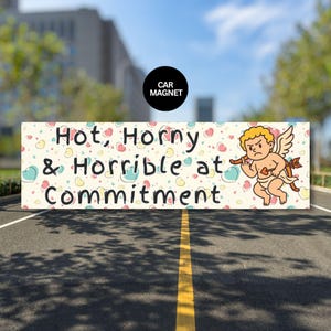 Puede incluir: Un imán rectangular para coche con el texto "Hot, Horny & Horrible at Commitment" en negro. El imán tiene un fondo crema con corazones coloridos y un cupido de dibujos animados con arco y flecha. Un círculo negro en la parte superior dice "CAR MAGNET".