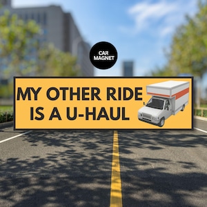 May include: A rectangular car magnet with the text "MY OTHER RIDE IS A U-HAUL" in black letters on a yellow background. A white U-Haul truck with red accents is on the right. A black circle with "CAR MAGNET" is in the upper center.