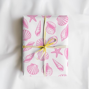 May include: A wrapped gift with white paper featuring a pink seashell pattern. The gift is tied with a yellow ribbon. The design includes various seashell illustrations and starfish.