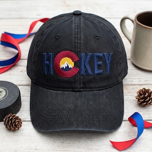 May include: A white ceramic mug with a black handle and the text "But First, Coffee" in a handwritten style. The mug is on a white surface. The mug is approximately 10 cm tall.