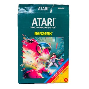 May include: A rectangular Atari Video Computer System game box for Berzerk featuring a dark green background with white text. The front displays a colorful illustration of a character in a futuristic setting and a yellow banner stating Comic Book.