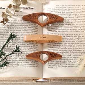 May include: Three wooden book page holders with a central circular cutout. The top and bottom holders are dark wood with engraved floral patterns. The middle holder is light wood with the name Jack engraved in script and small floral accents.