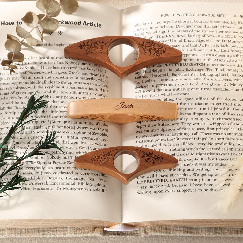 May include: Three wooden book page holders with a central circular cutout. The top and bottom holders are dark wood with engraved floral patterns. The middle holder is light wood with the name Jack engraved in script and small floral accents.