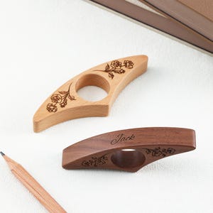 May include: Two wooden book page holders with a central hole for a thumb. The lighter wood holder features an engraved rose design. The darker wood holder features an engraved rose design and the name Jack in a cursive script font.