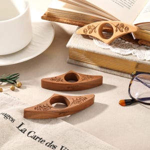 May include: Three wooden book page holders with a central circular opening. Each piece features a laser-engraved floral design on the top surface and the name Jack engraved on the front edge. The holders are crafted from smooth, light and dark wood.