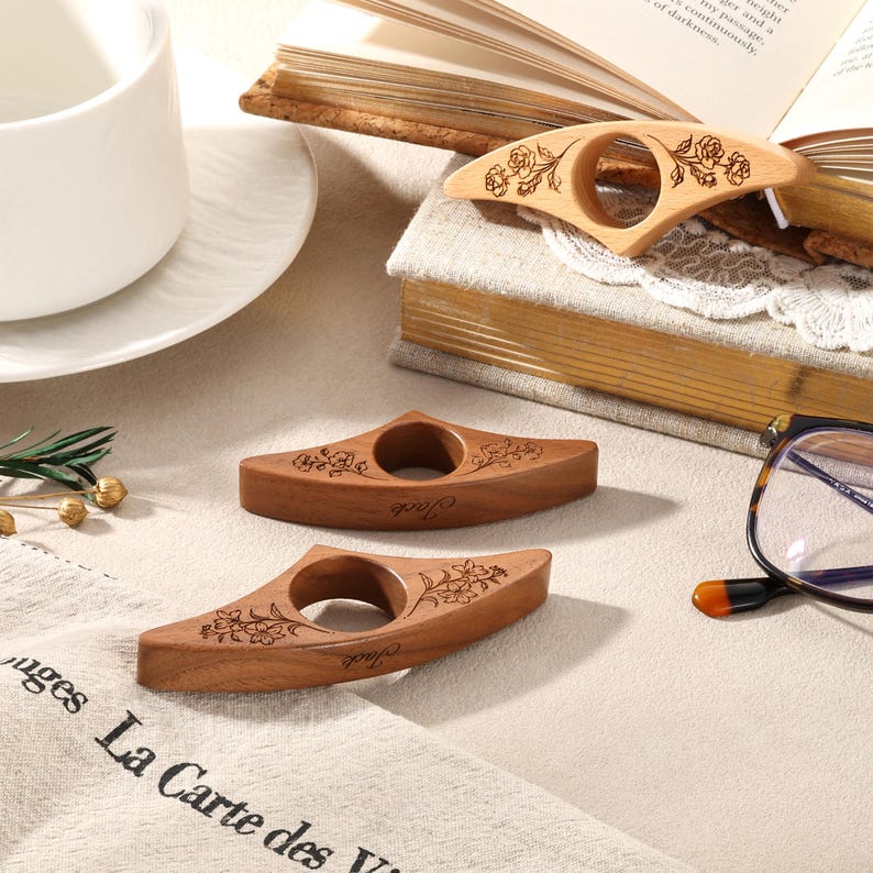May include: Three wooden book page holders with a central circular opening. Each piece features a laser-engraved floral design on the top surface and the name Jack engraved on the front edge. The holders are crafted from smooth, light and dark wood.
