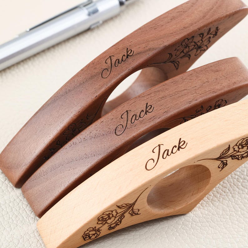 May include: Three wooden yarn bowls or yarn guides with a curved, elongated shape and a central circular opening. Each piece is engraved with the name Jack in a cursive script and features a detailed floral illustration on the wood surface.