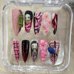May include: A set of ten artificial nails with various designs. The nails feature a range of colors, including pink, red, black, and white. Some nails have floral and character designs, while others have abstract patterns and a spiderweb design.