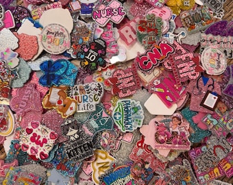 May include: A large collection of colorful, glittery acrylic badges and charms featuring medical themes. Designs include text like Nurse, CNA, FNP, Pharmacy, and Medical Assistant, alongside illustrations of stethoscopes, hearts, and medical characters.