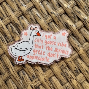 May include: A rectangular pin with a white goose illustration and the text "I got a silly goose vibe that the serious geese don't appreciate." The pin has a pink glitter border and a pink bow on the goose.