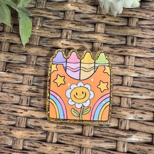 May include: A colorful, glitter-edged pin featuring a smiling flower, rainbows, stars, and crayons. The pin has an orange background and is a fun, whimsical accessory.
