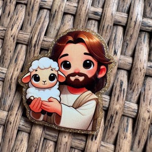 May include: A glittery sticker featuring a cartoon illustration of a figure with brown hair and a beard holding a lamb. The figure is wearing a white robe with a tan sash. The sticker has a gold glitter border.