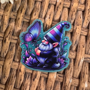 May include: A whimsical sticker featuring a gnome with a long white beard and a striped hat, holding a flower for a butterfly. The design is in shades of purple, blue, and teal, with a glittery finish.