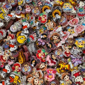 May include: A large collection of colorful acrylic charms featuring various cartoon characters, including Pikachu, Snoopy, Ariel, and Hello Kitty. The charms are flat, glossy, and display diverse shapes and vibrant printed designs.