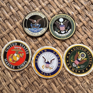 May include: Five circular challenge coins featuring emblems of the United States military branches. The coins display the Navy, Army, and Marine Corps insignias with eagles, anchors, and shields in black, green, red, blue, and gold metallic colors.