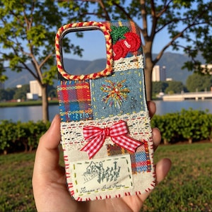 Może przedstawiać: Etui na telefon z patchworkiem z czerwoną i białą kokardą w kratkę, haftowanymi detalami i przyszytą etykietą. Etui posiada różnorodne tkaniny, w tym dżins i kratę, z dekoracyjną czerwoną i białą plecioną obwódką wokół obiektywu.